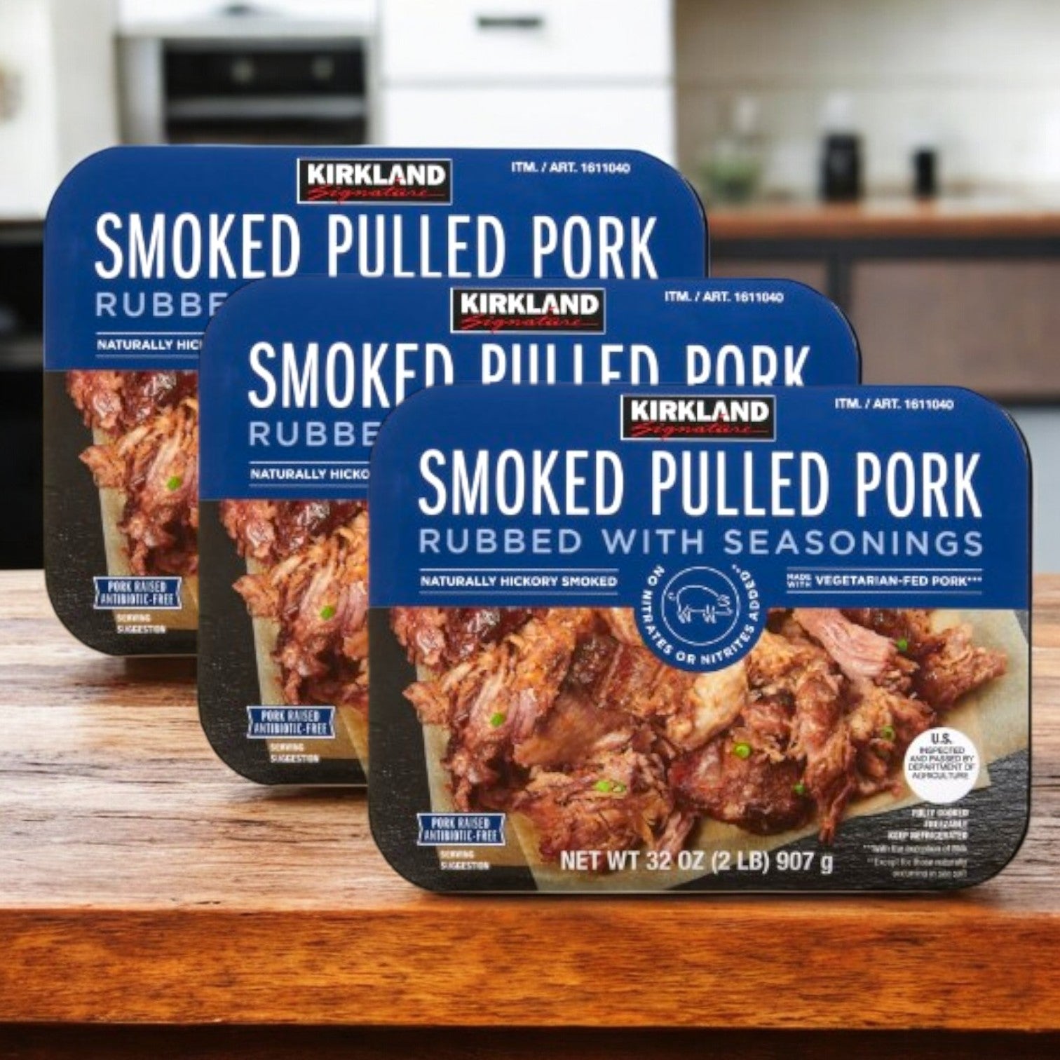 Three 32 oz cases of Kirkland Signature Smoked Pulled Pork, rubbed with seasonings, are shown on a wooden surface. The packaging emphasizes savory seasoning and hickory smoked BBQ flavor.