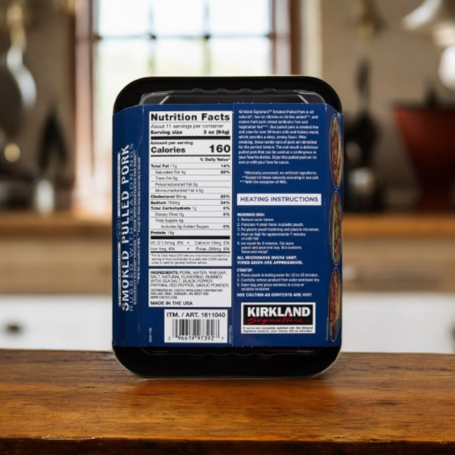 A 32 oz container of Kirkland Signature Smoked Pulled Pork, rubbed with seasonings, sits on the counter with its nutrition facts and heating instructions clearly visible on the label.
