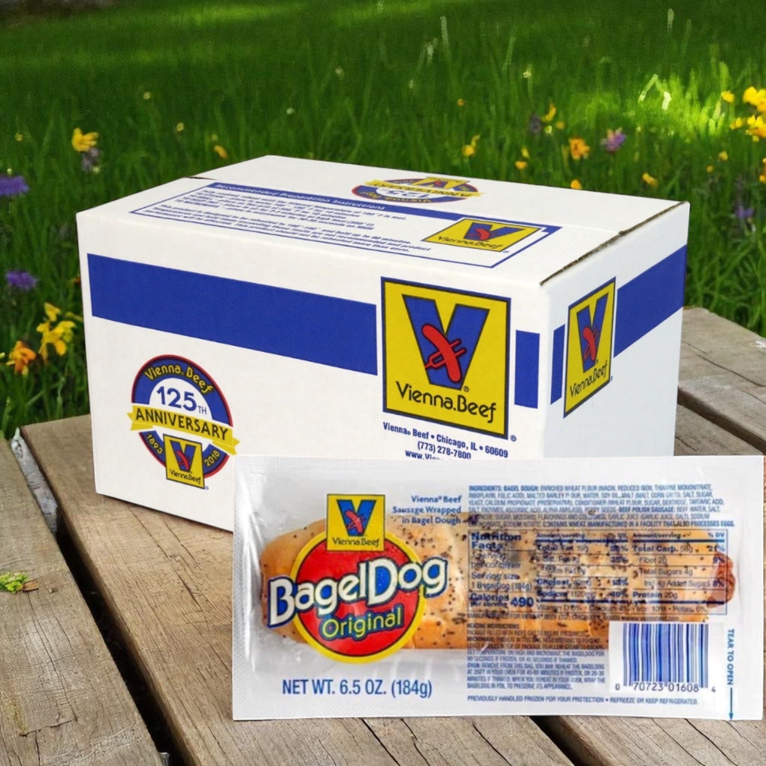A Vienna Beef BagelDog – 6.5 oz. - 24 Total box and its packaging are shown on a wooden surface outdoors, highlighting this classic Chicago bagel-wrapped hot dog by Vienna Beef with grass and flowers in the background.