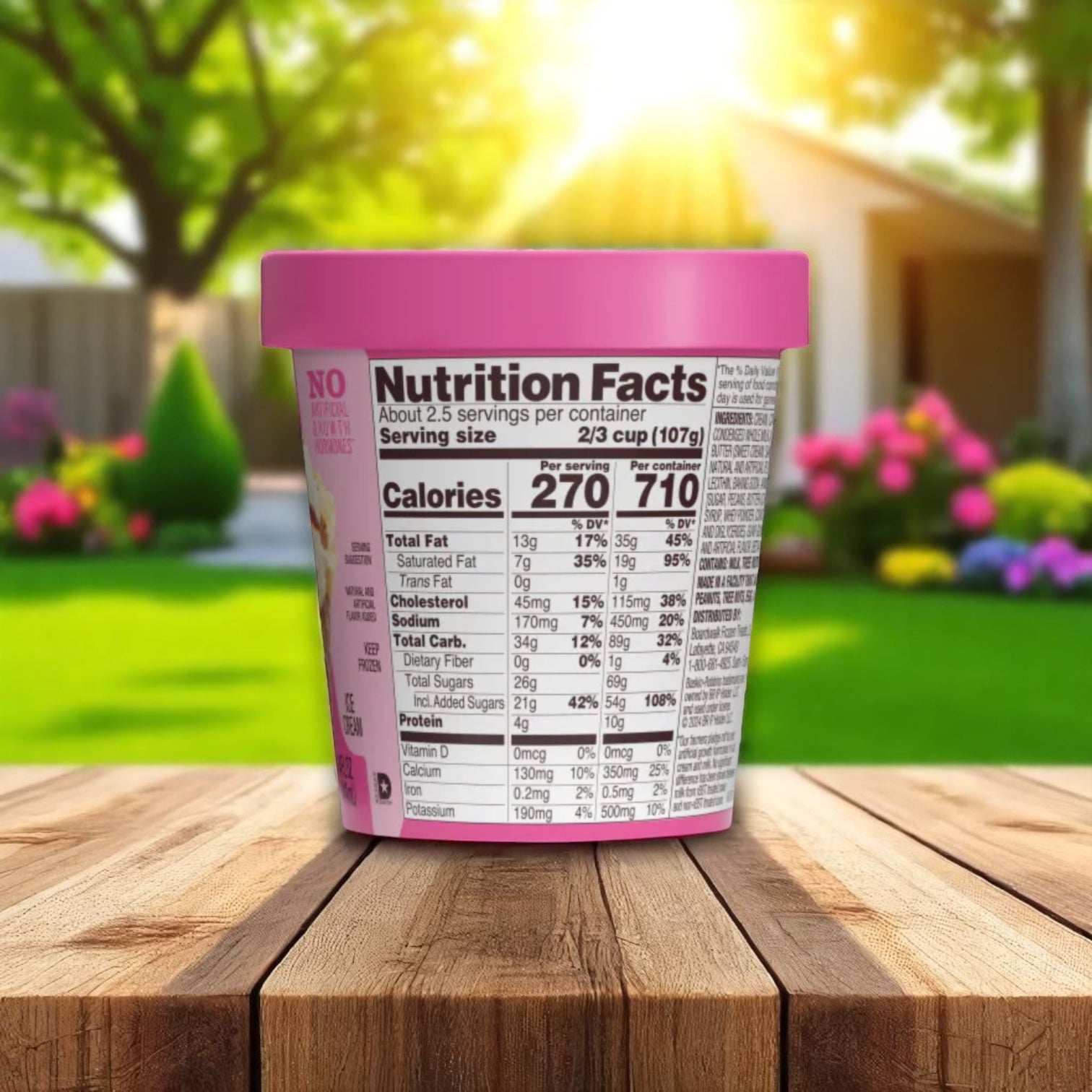 A pink Easy Lunches Baskin Robbins Pralines 'N Cream ice cream container (14 oz, vanilla with praline-coated pecan pieces) sits outdoors on a wooden table, nutrition facts visible, with a blurred garden and house in the background.