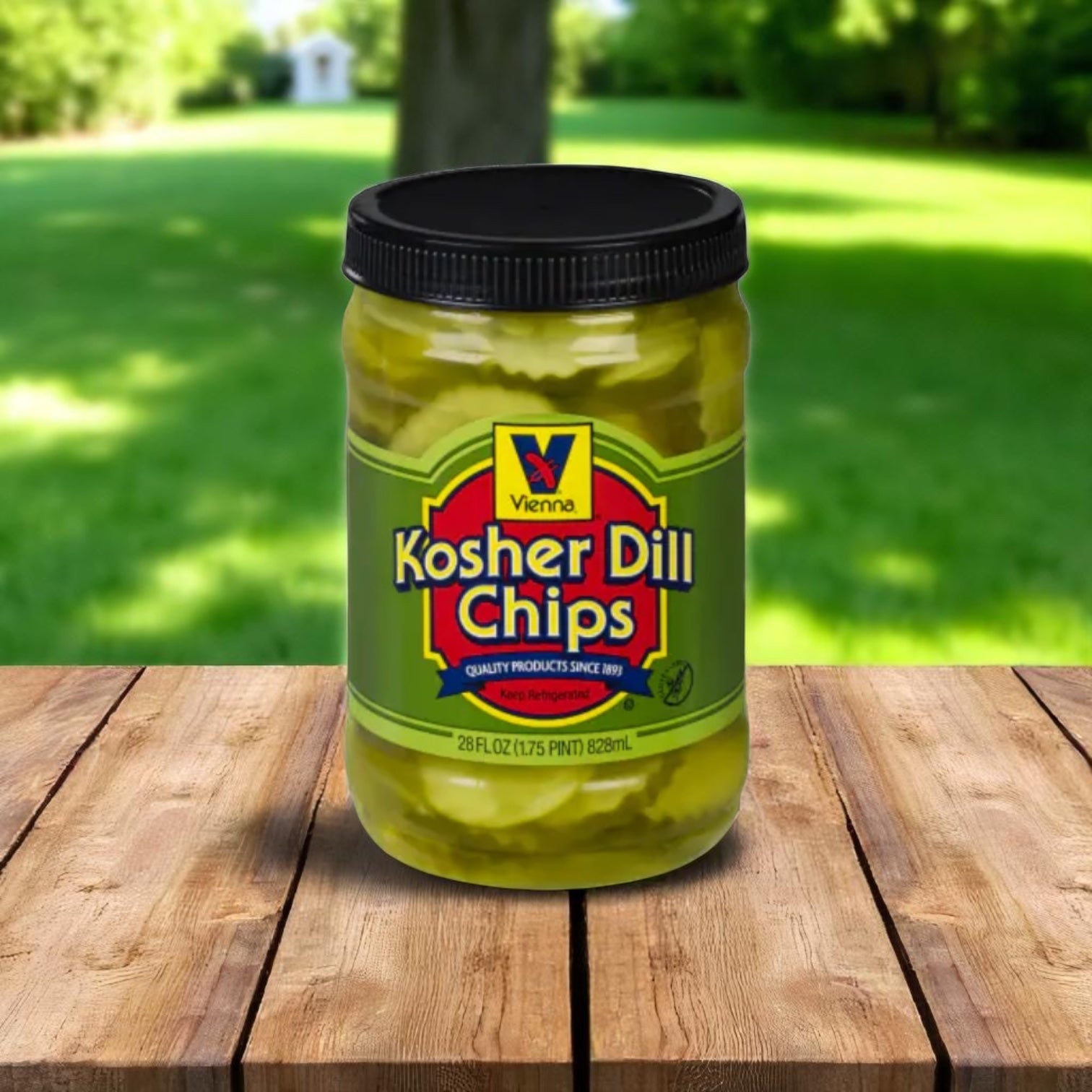 A jar of Easy Lunches Vienna Kosher Dill Pickle Chips sits on a wooden surface outdoors, with green grass and trees blurred in the background.
