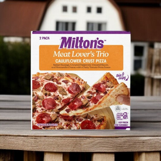 A box of Milton’s Meat Lover’s Cauliflower Crust Pizza, 17.5 oz, 2-count by Milton’s is displayed outdoors with a barn in the background.