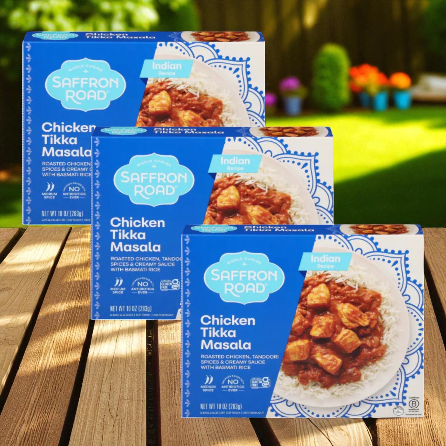 Three boxes of Saffron Road® Chicken Tikka Masala with Basmati Rice Gluten-Free Frozen Dinner (3 Count) are displayed outdoors on a wooden surface, promising a convenient and flavorful Indian meal from Saffron Road.