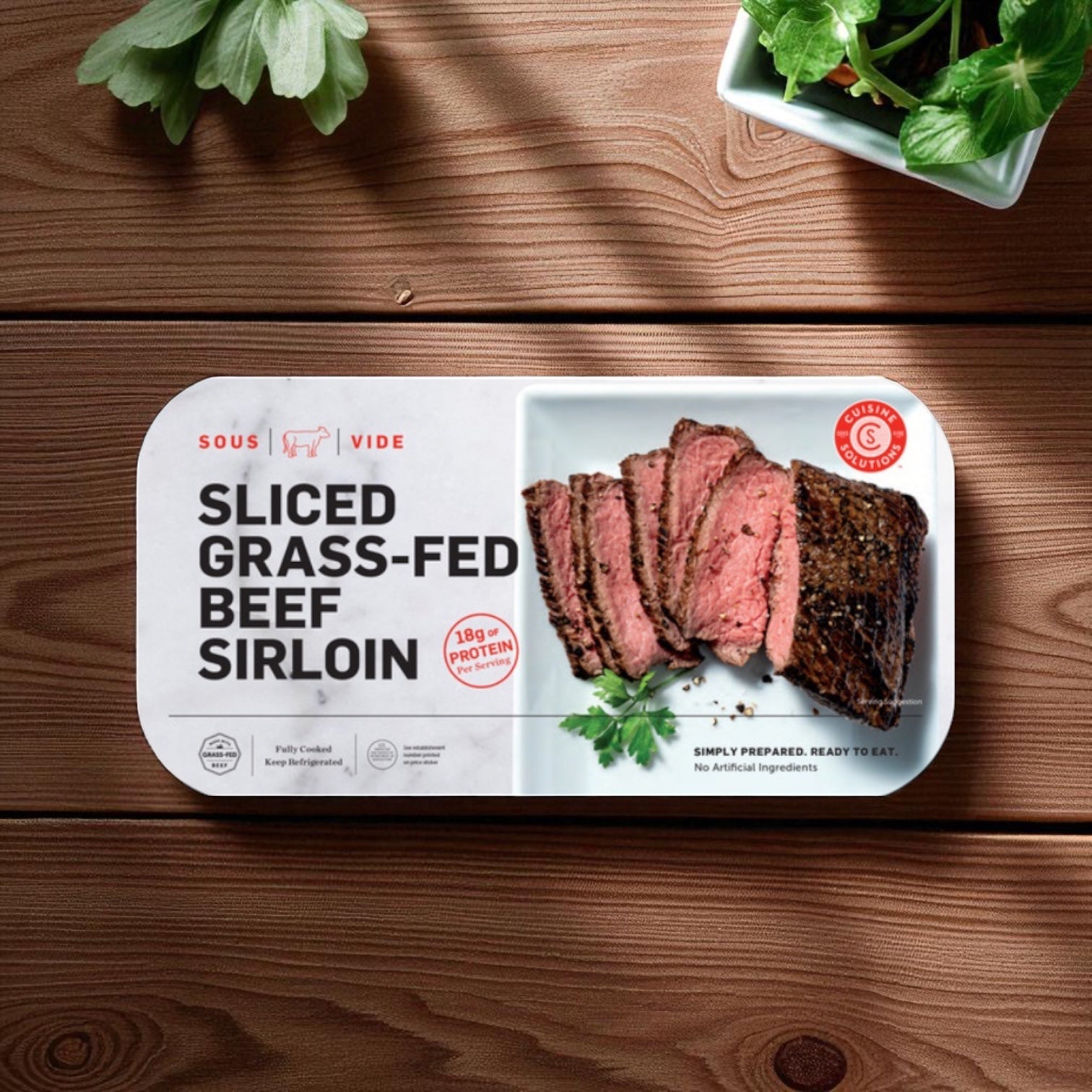 Cuisine Solutions Sliced Grass-Fed Beef Sirloin, 1-count, shown on wood with herbs. The label highlights 18g protein per serving, fully cooked beef, simple prep, and no artificial ingredients.