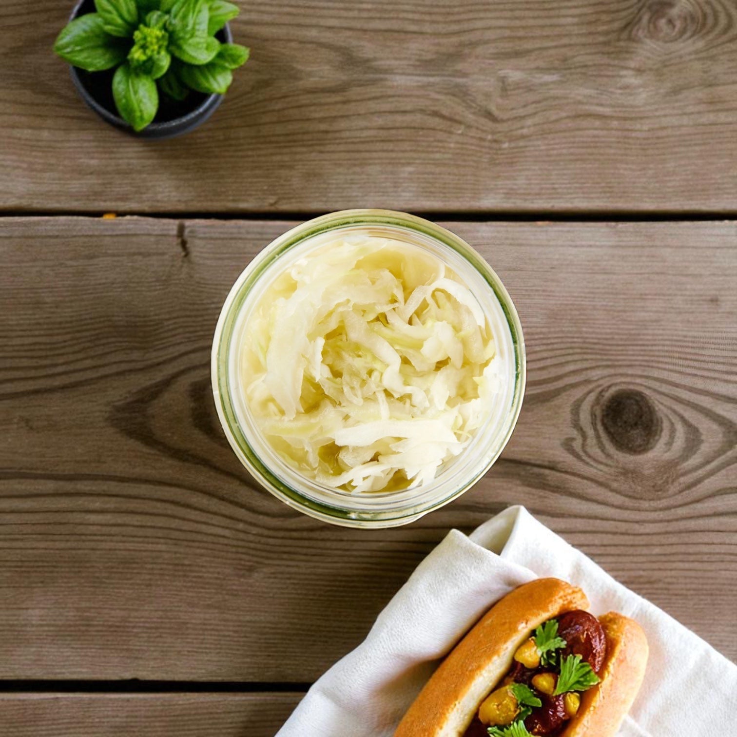 A jar of Vienna Beef Sauerkraut sits on a wooden table beside a hot dog topped with Chicago-style green relish, with a small potted plant nearby.