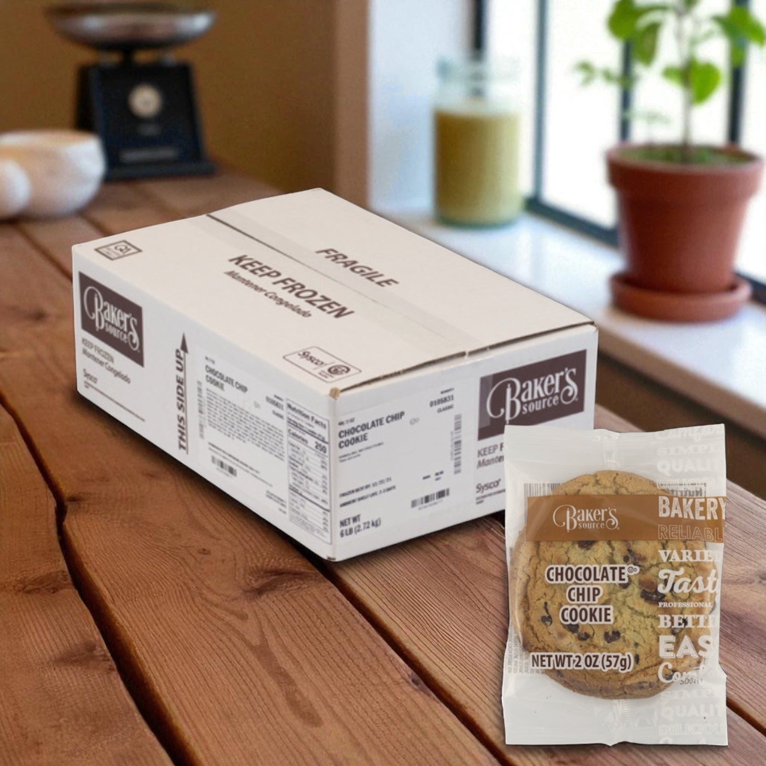 A box labeled "Baker's Source Classic" sits on a wooden table, with a single 2 oz chocolate chip cookie from their 48-count individually wrapped bulk pack displayed in the foreground.