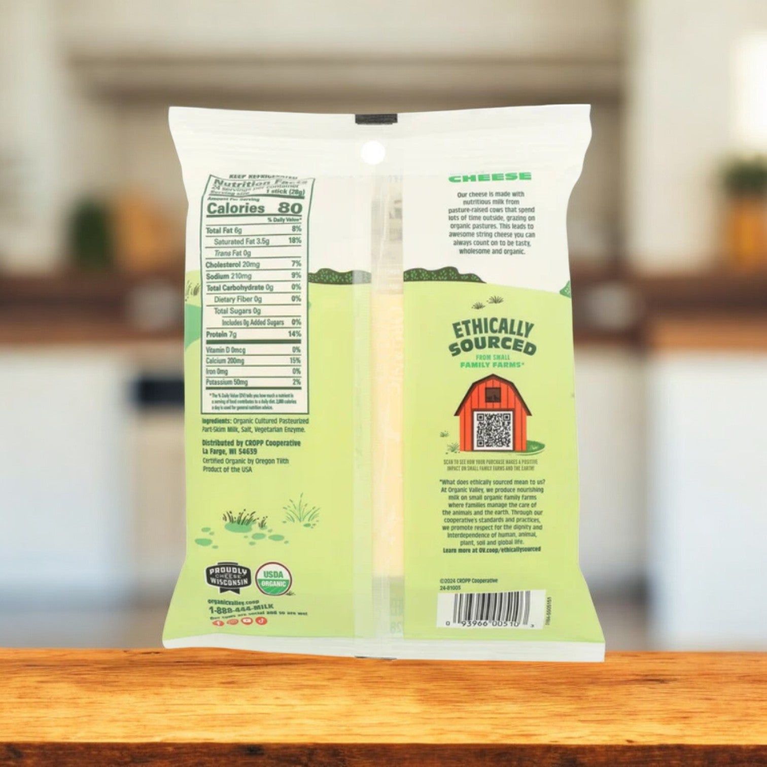 A bag of Organic Valley Stringles Organic String Cheese (24 sticks, 24 oz) sits on a wooden kitchen surface, with nutritional info on the left and an "Ethically Sourced" barn-illustrated label and QR code on the right.