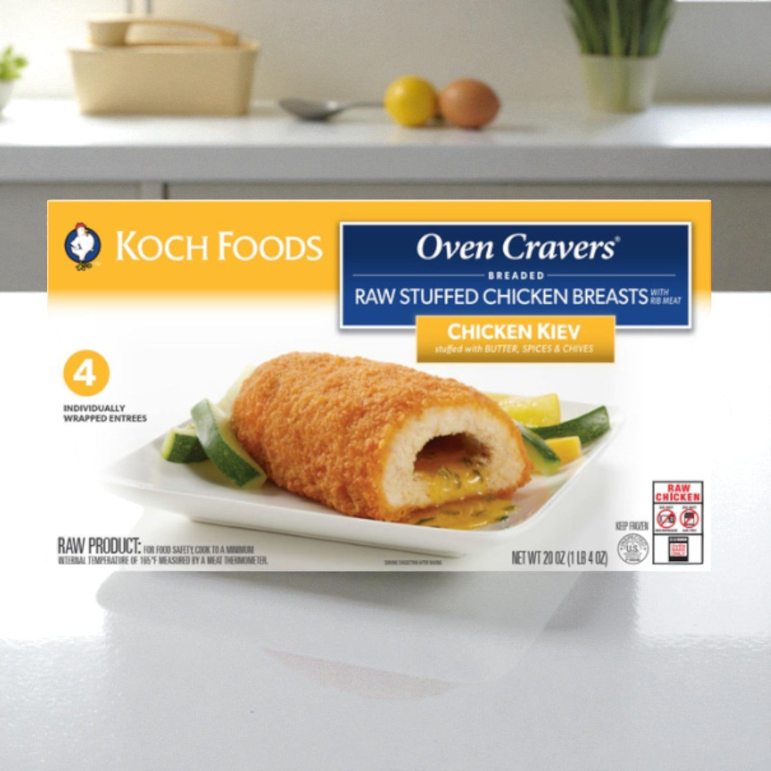 A box of Koch Foods Chicken Kiev Breaded Raw Stuffed Chicken Breasts with Rib Meat (20 oz, 4 pieces per case) is displayed on a white counter, with the cooked chicken served on a plate alongside vegetables.