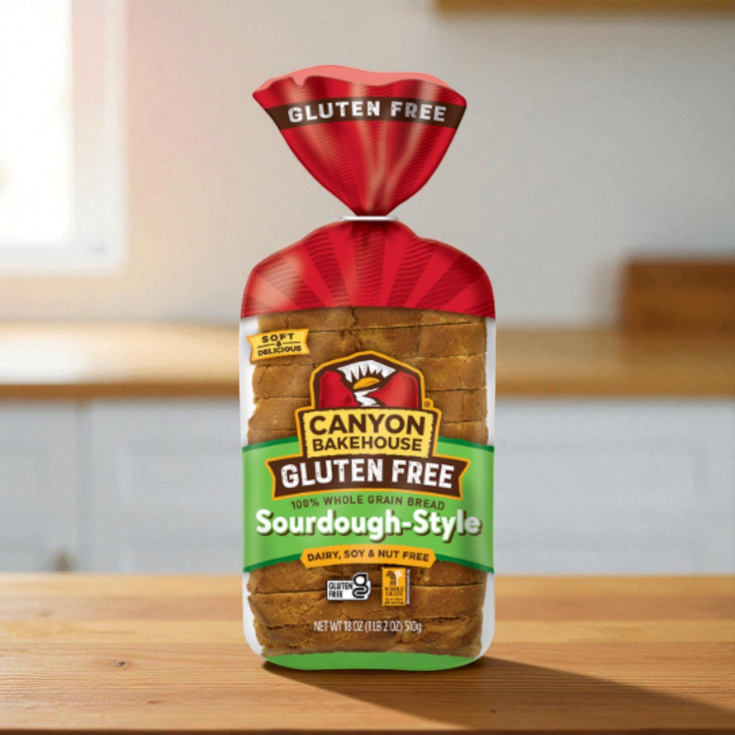 A bag of Canyon Bakehouse Bread, 100% Whole Grain, Gluten Free, Sourdough-Style (18 oz) sits on a wooden surface with a blurred kitchen backdrop.