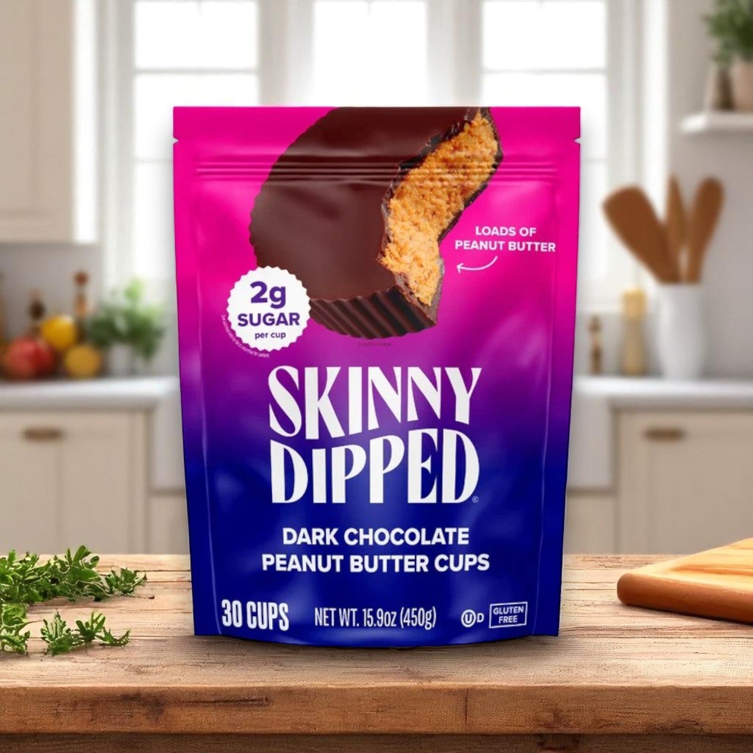 A package of Skinny Dipped Cups, Dark Chocolate Peanut Butter, 30-Count by Skinny Dipped is displayed on a kitchen counter, showcasing its low sugar content and product highlights.