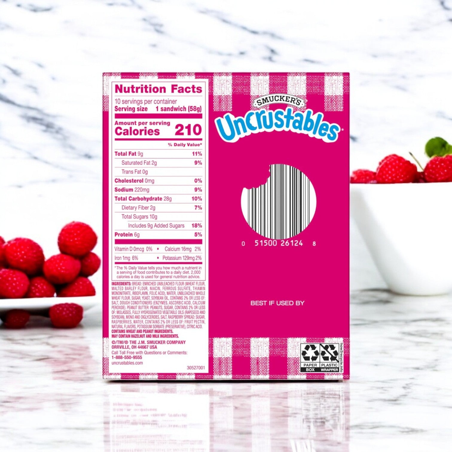 A box of Uncrustable Smuckers Peanut Butter & Raspberry Spread Sandwiches (10 Pack, 2 oz each) sits on a white surface with raspberries nearby, showcasing its convenient snacking and visible nutrition facts label.