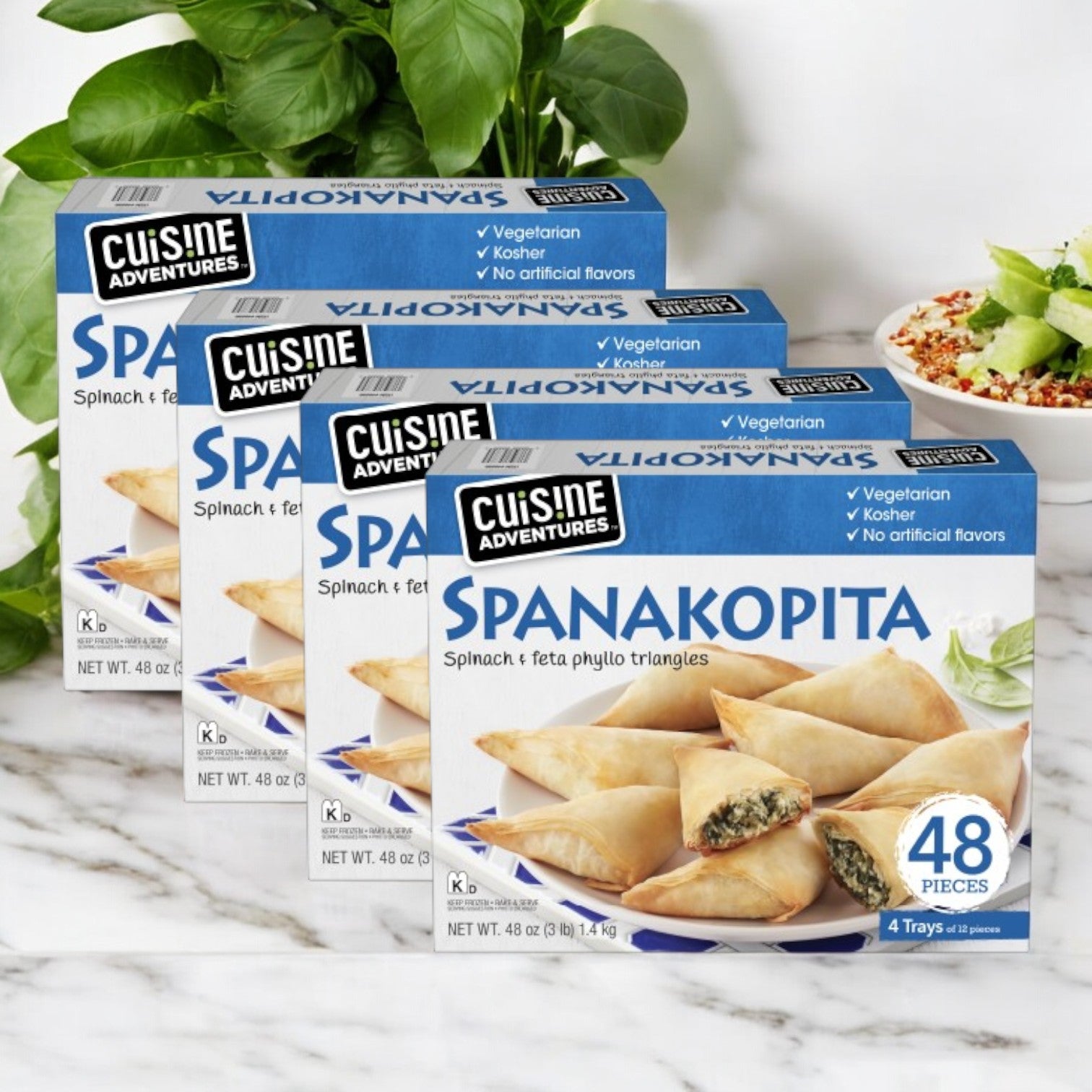 Four boxes of Cuisine Adventures Spanakopita Spinach & Feta Phyllo Triangles are beautifully displayed with a basil plant and a fresh salad. Each box offers 48 delicious phyllo triangles, ideal for any event.