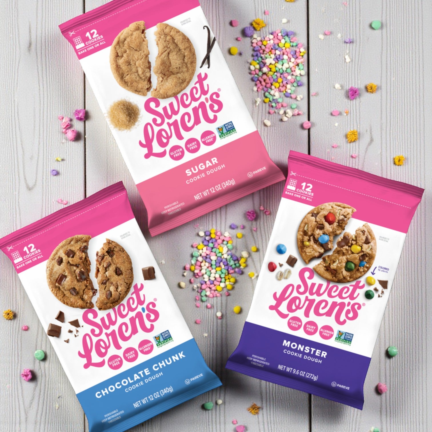 Three Sweet Loren’s Cookie Dough packs—Monster (9.6 oz), Chocolate Chunk (12 oz, Gluten-Free & Vegan), and Sugar Cookie (12 oz, Gluten-Free & Vegan)—are displayed on a wooden surface with colorful sprinkles scattered around.