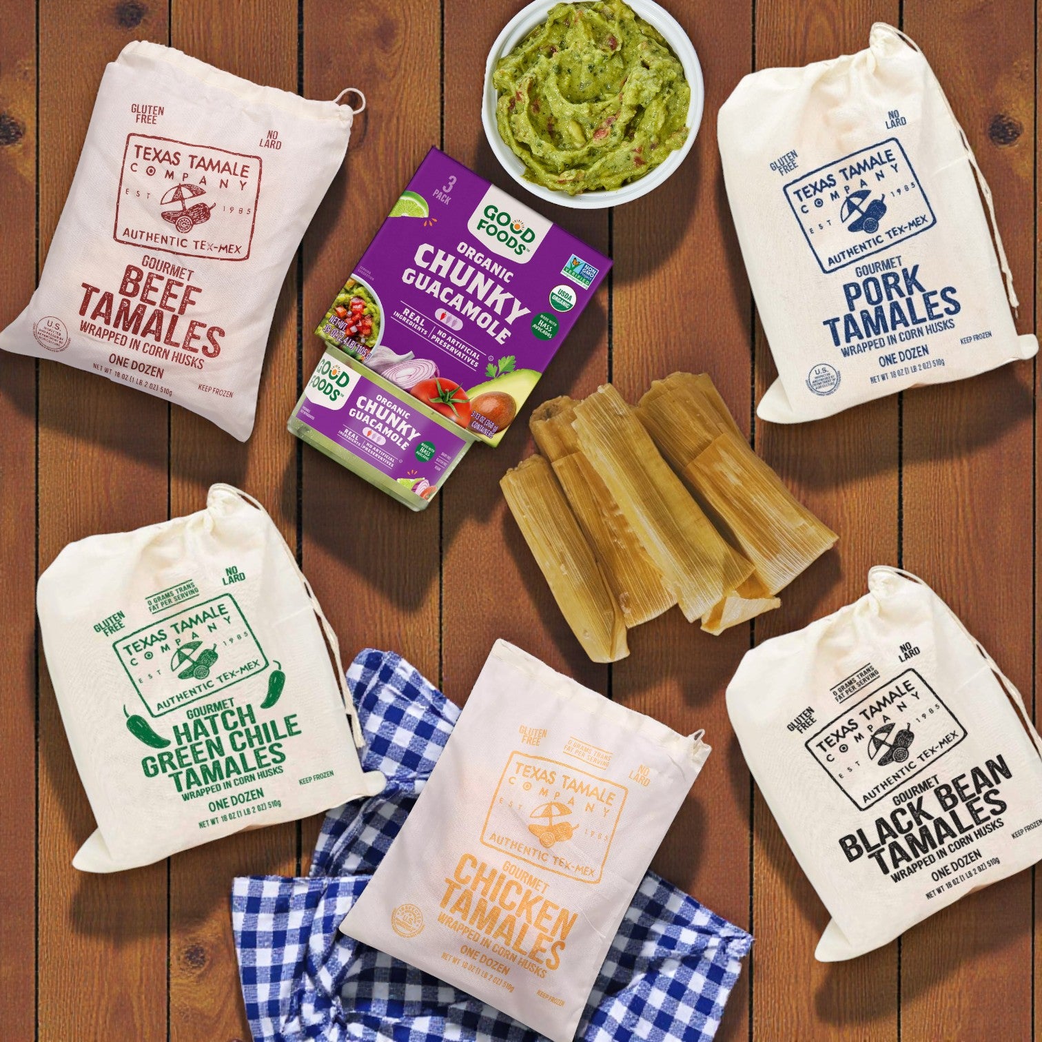 The Combo Pack featuring Texas Tamale Company Tamale Fiesta (6 Dozen) and Good Foods Organic Chunky Guacamole is displayed on a wooden surface with a blue-checked napkin.
