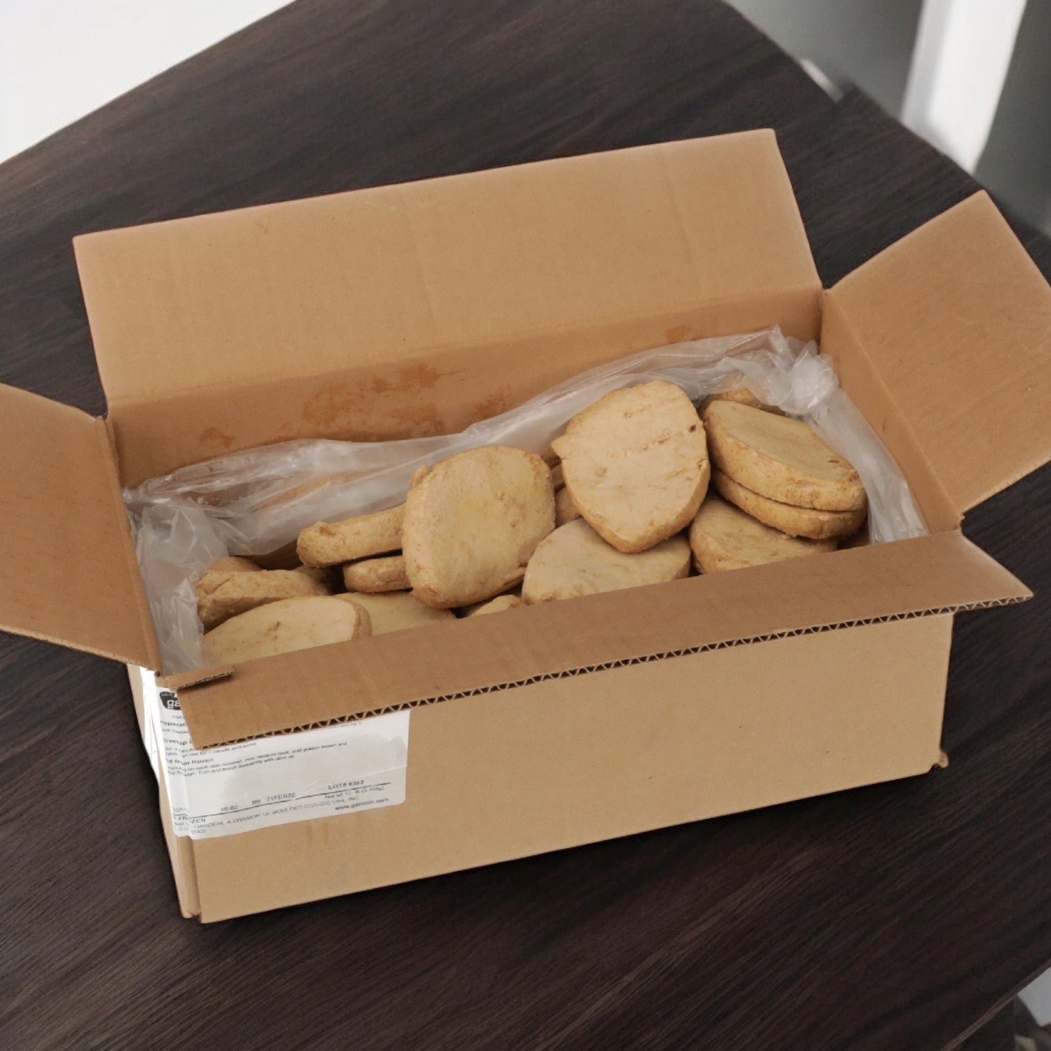 An open cardboard box displays Gardein's plant-based veggie burger chicken breasts, lined with plastic on a dark wood surface, offering a delightful treat.