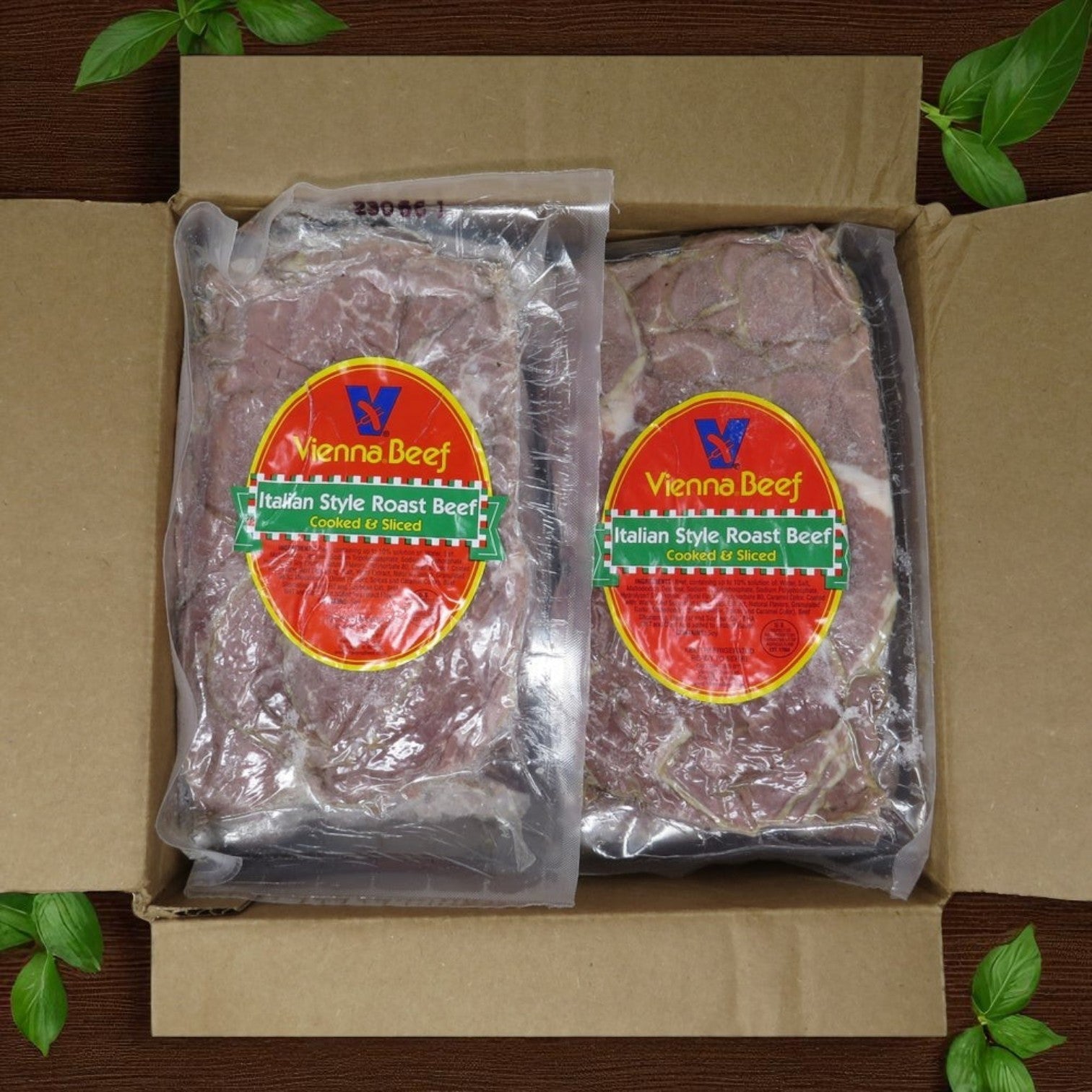 Two vacuum-sealed packs of Vienna Beef Italian Style Roast Beef from a 30-pound case are arranged in an open cardboard box, surrounded by fresh green basil leaves.