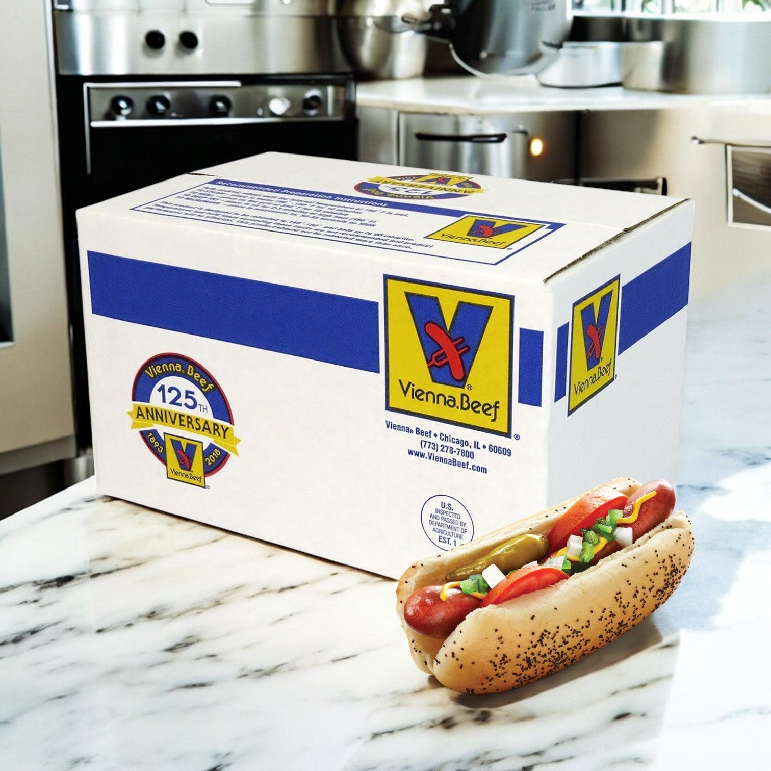 A Vienna Beef Natural Casing Hot Dog – 6" sits in a poppy seed bun with toppings on a marble counter next to a Vienna Beef 125th anniversary shipping box, highlighting the classic taste of this authentic brand in a kitchen setting.