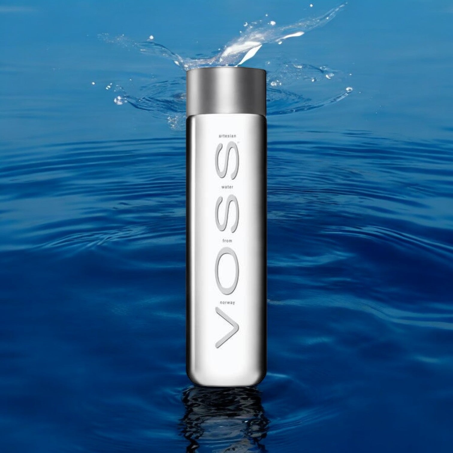 A VOSS Still Water, 28.7 fl oz bottle, plunges into calm blue water, sending droplets upward—a fitting image for the pure artesian quality of VOSS’s premium 6 Pack offering.