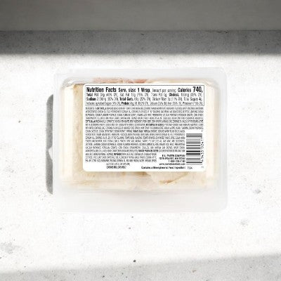 A plastic E.A. Sween Italian Style Wrap container (1 case, 8 count; ships frozen; 30 days shelf life in cooler) sits on a white surface in sunlight, showing its nutrition label listing 740 calories per serving.