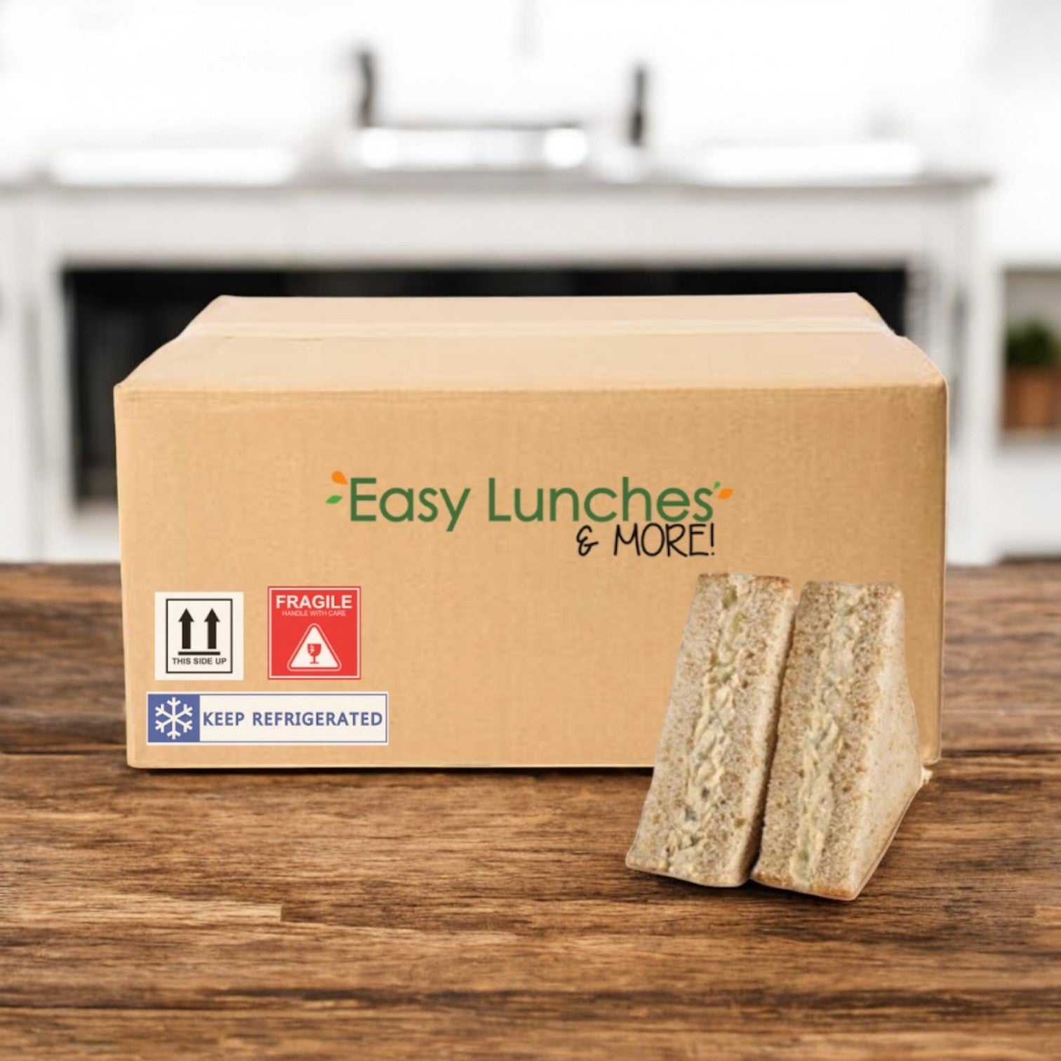 A cardboard box labeled "E.A. Sween Albacore Tuna Salad Sandwich-1 Case, 8 Count" sits on a wooden surface, with two sandwich halves—filled with creamy tuna salad—displayed in front. Ships frozen; 30 days shelf life in the cooler.