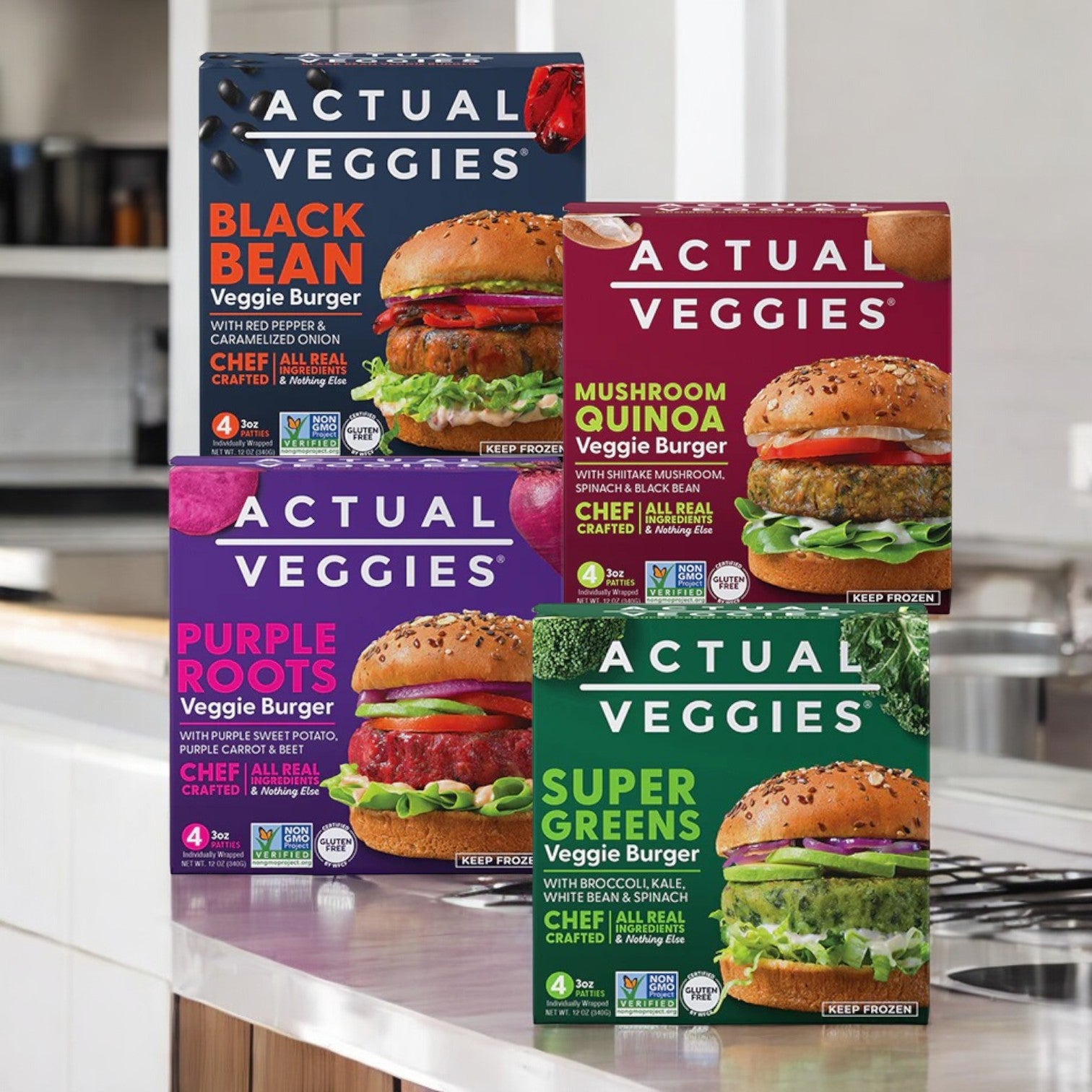 Four packs from the Actual Veggies 4 Pack Bundle are displayed on a kitchen counter, featuring four delicious veggie burger varieties: Black Bean, Mushroom Quinoa, Purple Roots, and Super Greens.