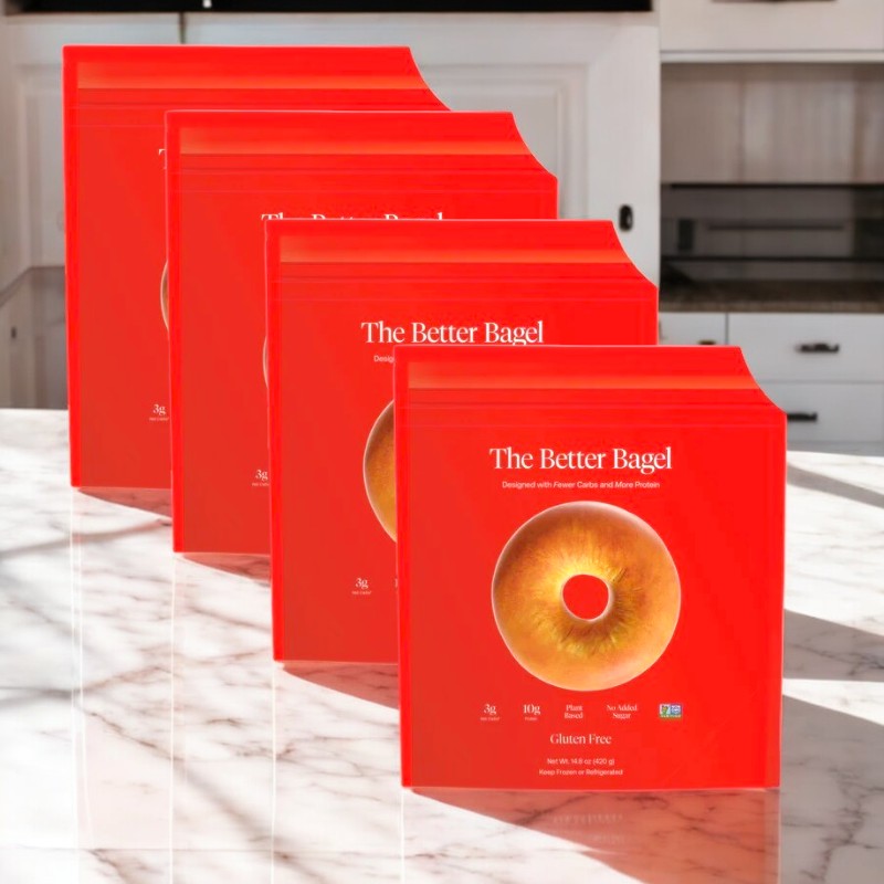 Four packages of "BetterBrand - The Gluten Free Better Bagel" are arranged in a row on a marble countertop in a well-lit kitchen setting.