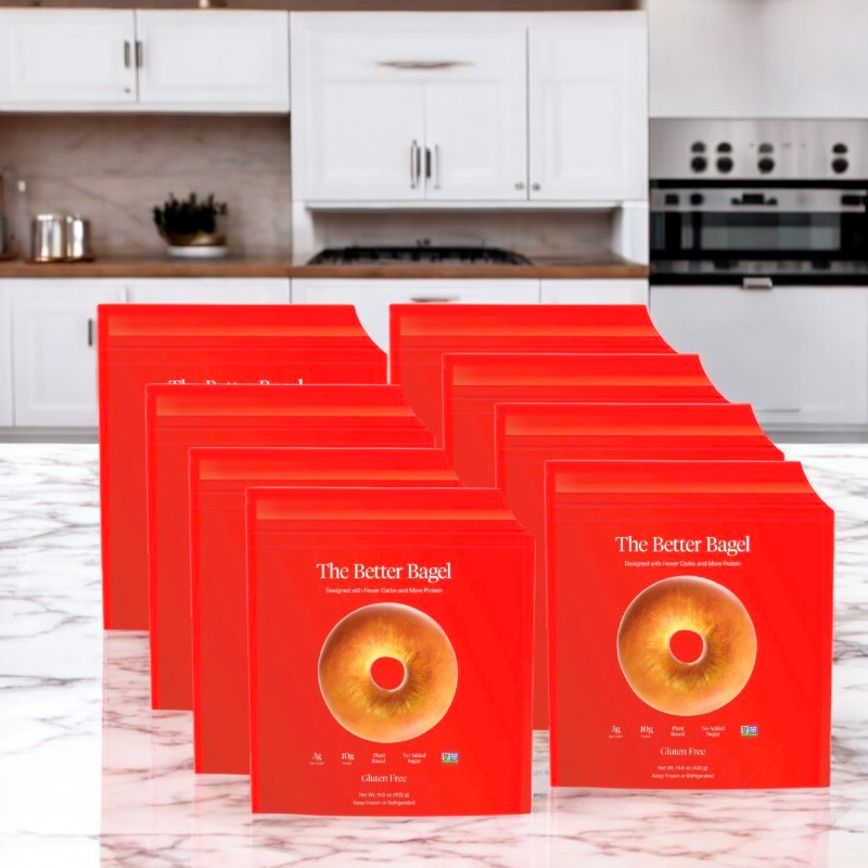 Boxes of "Better Brand - The Gluten Free Better Bagel," featuring bright red packaging with a tempting bagel image, are neatly arranged on a kitchen counter in front of a modern backdrop.