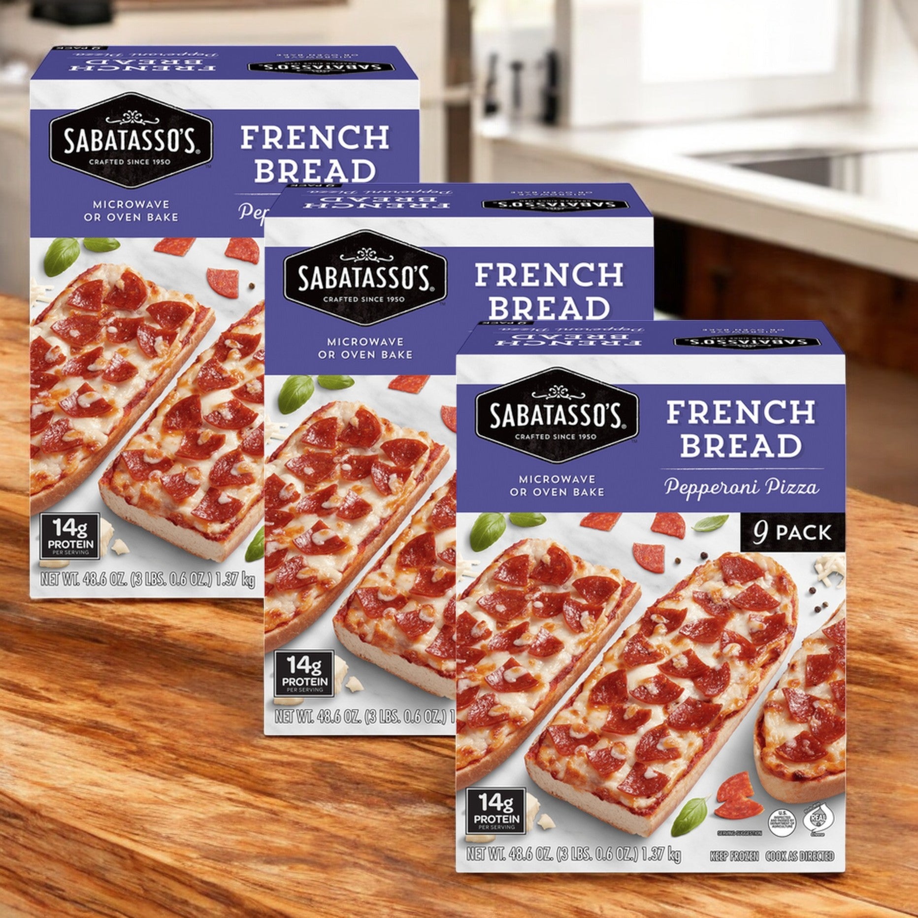 Three boxes of Sabatasso's French Bread Pepperoni Pizza, 48.6 oz. each, are displayed on a wooden counter, showing appetizing images and labeled as a 3-pack by Sabatasso's.