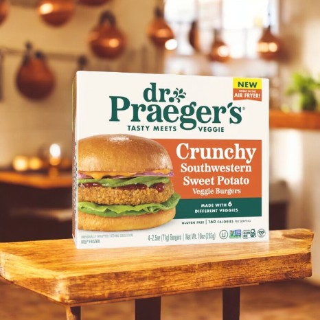 A box of Dr. Praegers Veggie Burgers, Crunchy Southwestern Sweet Potato flavor, made from plant-based ingredients and gluten-free, is attractively placed on a wooden table in a cozy kitchen setting.