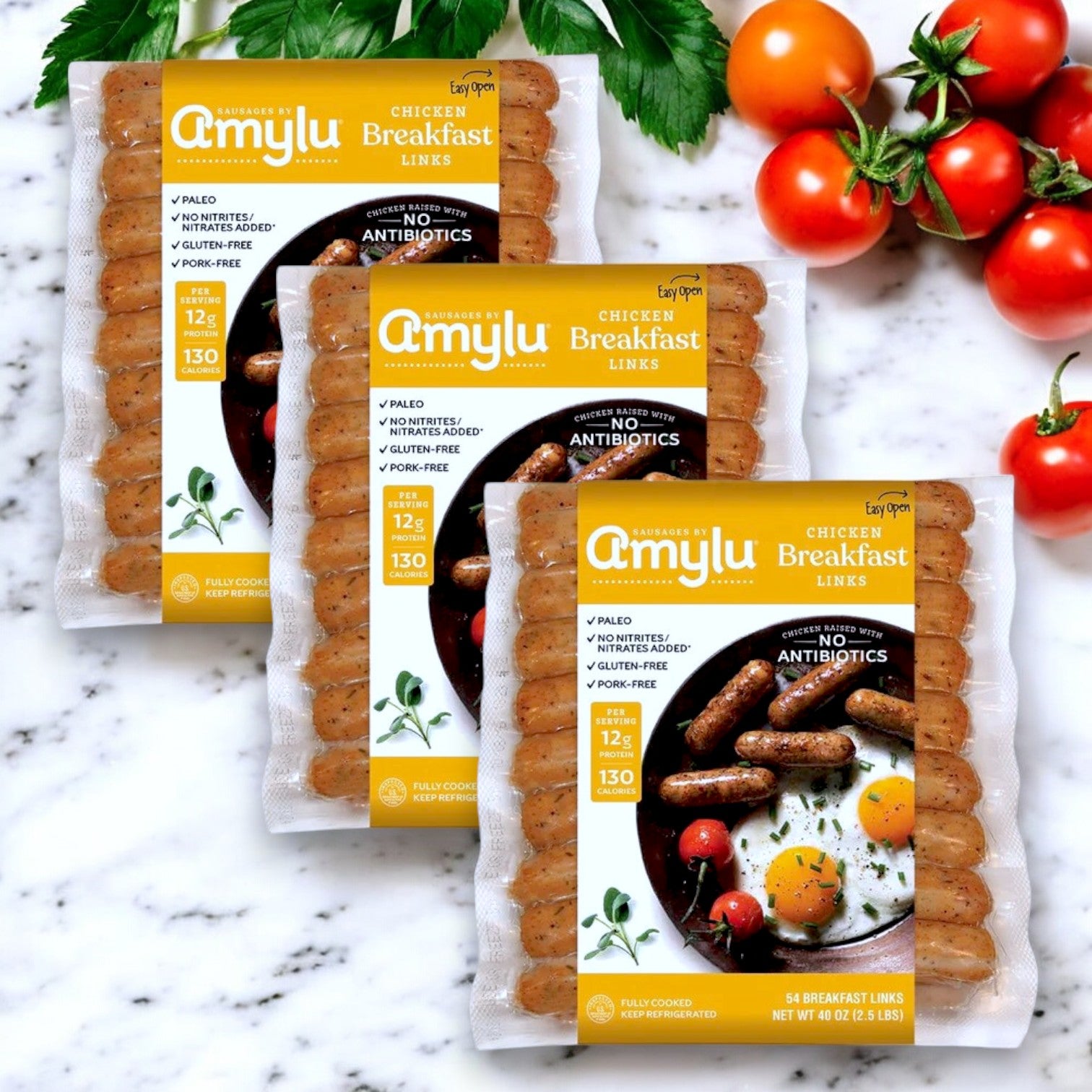 Three packs of Amylu Chicken Breakfast Sausage Links – 7.5 lbs are arranged on a white surface, surrounded by cherry tomatoes and herbs, displaying their gluten-free, keto, and paleo-friendly attributes alongside nutritional information.