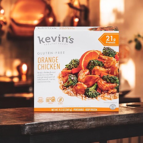 A box of Kevin's Natural Foods Orange Chicken-1 Count sits on a kitchen counter, featuring packaging from the Kevin's brand with a photo of chicken, broccoli, and rice.