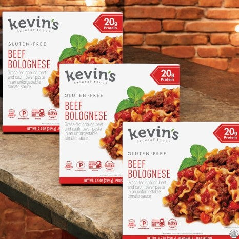 Three boxes of Kevin's Natural Foods Beef Bolognese- 3 Count, a keto-friendly and gluten-free meal from Kevin's, are displayed on a wooden surface with a brick wall in the background.