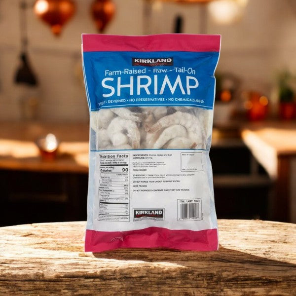 A bag of Kirkland Signature Farm-Raised Raw Shrimp, Tail-On, Peeled, and Deveined is displayed on a wooden surface in a cozy kitchen.