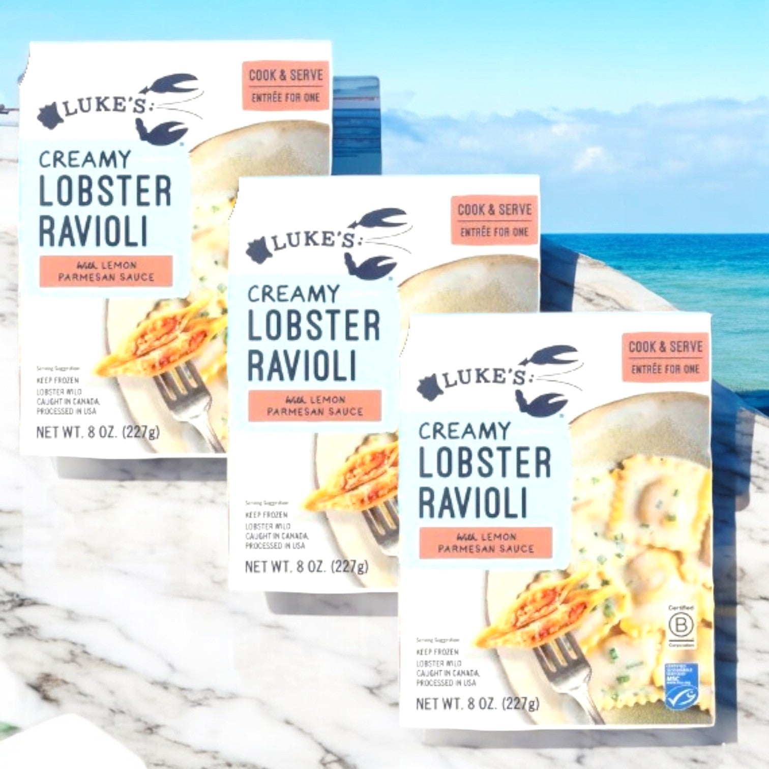 Three boxes of Luke's Creamy Lobster Ravioli-3 Count by Luke's, filled with creamy lobster and mild lemon parmesan sauce, offer a premium seafood experience as they’re set before a sunny ocean view.