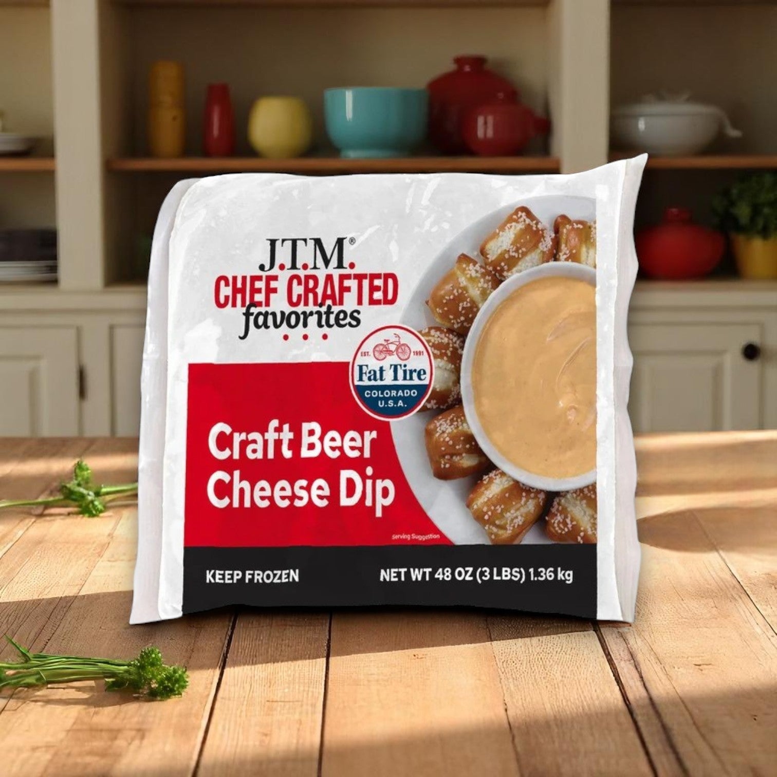 A 48 oz tub of J.T.M Craft Beer Cheese Dip is displayed on a wooden kitchen counter with shelves and dishes in the background—ideal for tasty party snacks.