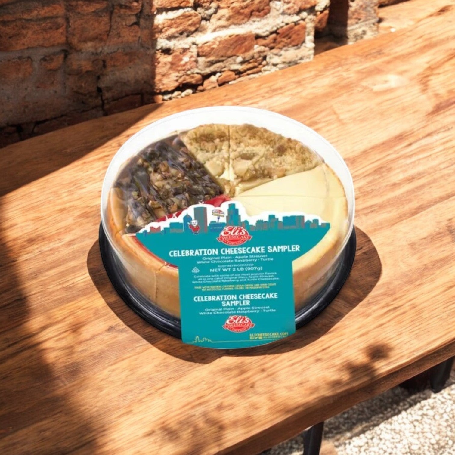 An Eli's Cheesecake Celebration Sampler & Home Run Inn Pizza Combo by Easy Lunches sits on a wooden table outdoors, near a brick wall—ideal for dessert lovers like Chicago-style pizza fans appreciate their deep dish.