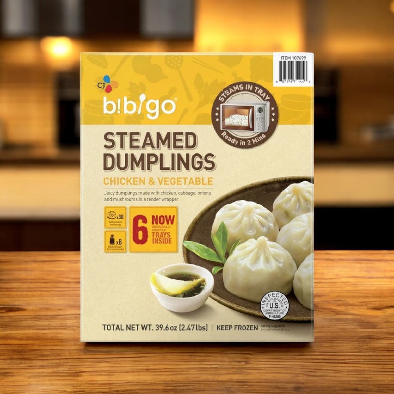A 39.6 oz box of Bibigo Steamed Dumplings, Chicken & Vegetable (18-count), sits on the counter; its packaging features easy microwave steam prep and six included trays.