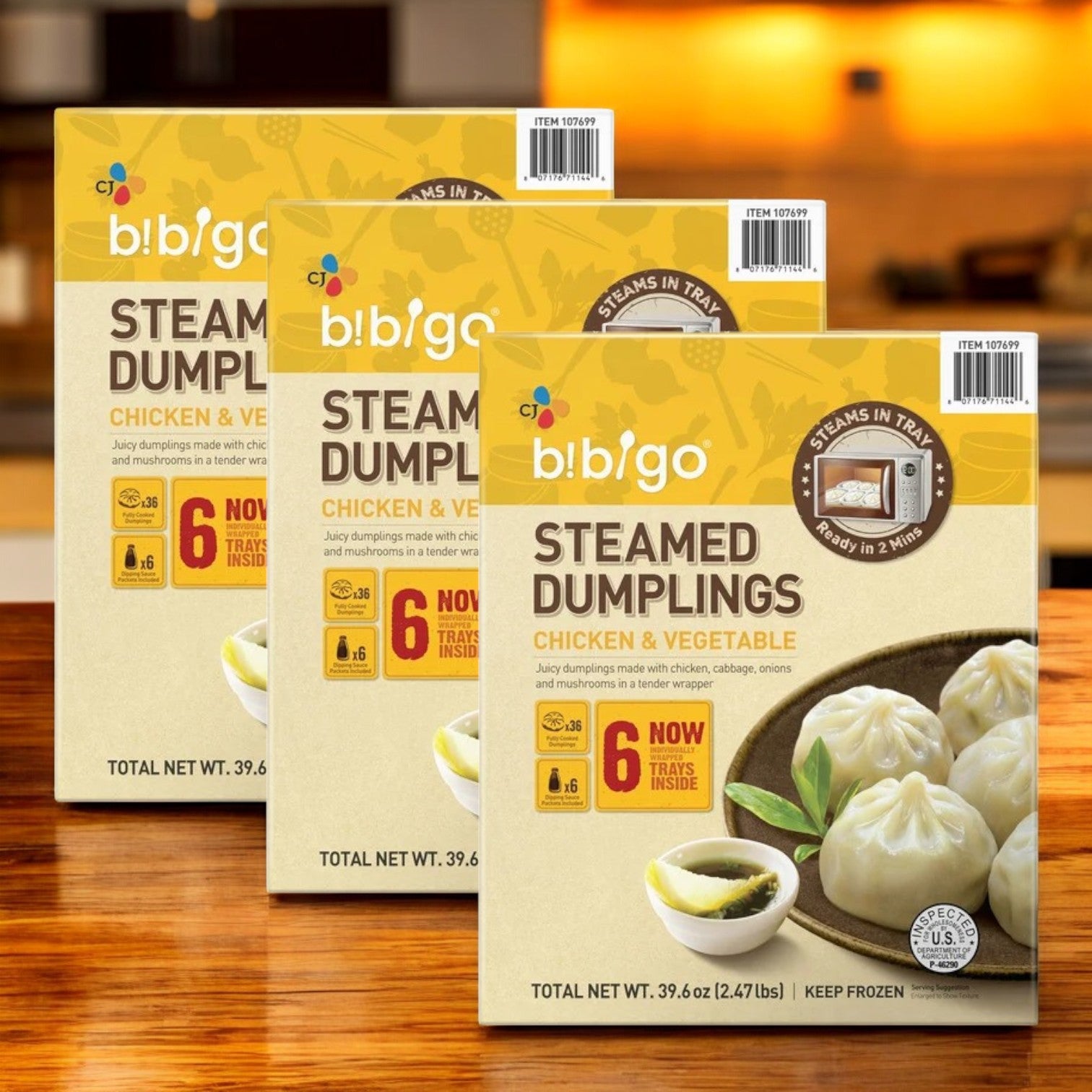 Three boxes of CJ Bibigo Steamed Dumplings, Chicken & Vegetable (39.6 oz, 18-count), are displayed on a wooden surface with a kitchen background.