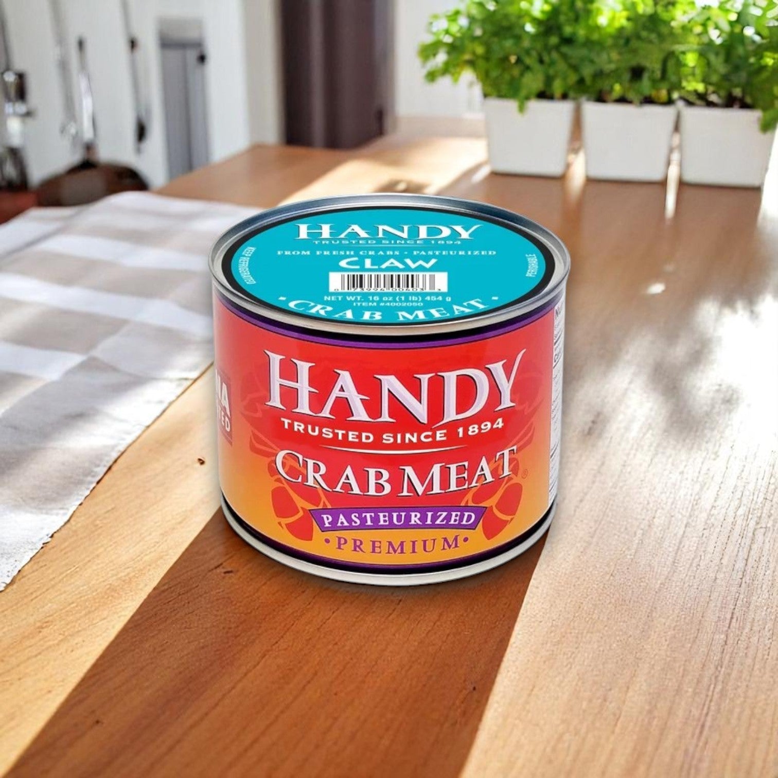 A 16 oz can of Handy Claw Crab Meat rests on a wooden table lit by sunlight, with plants in the background.
