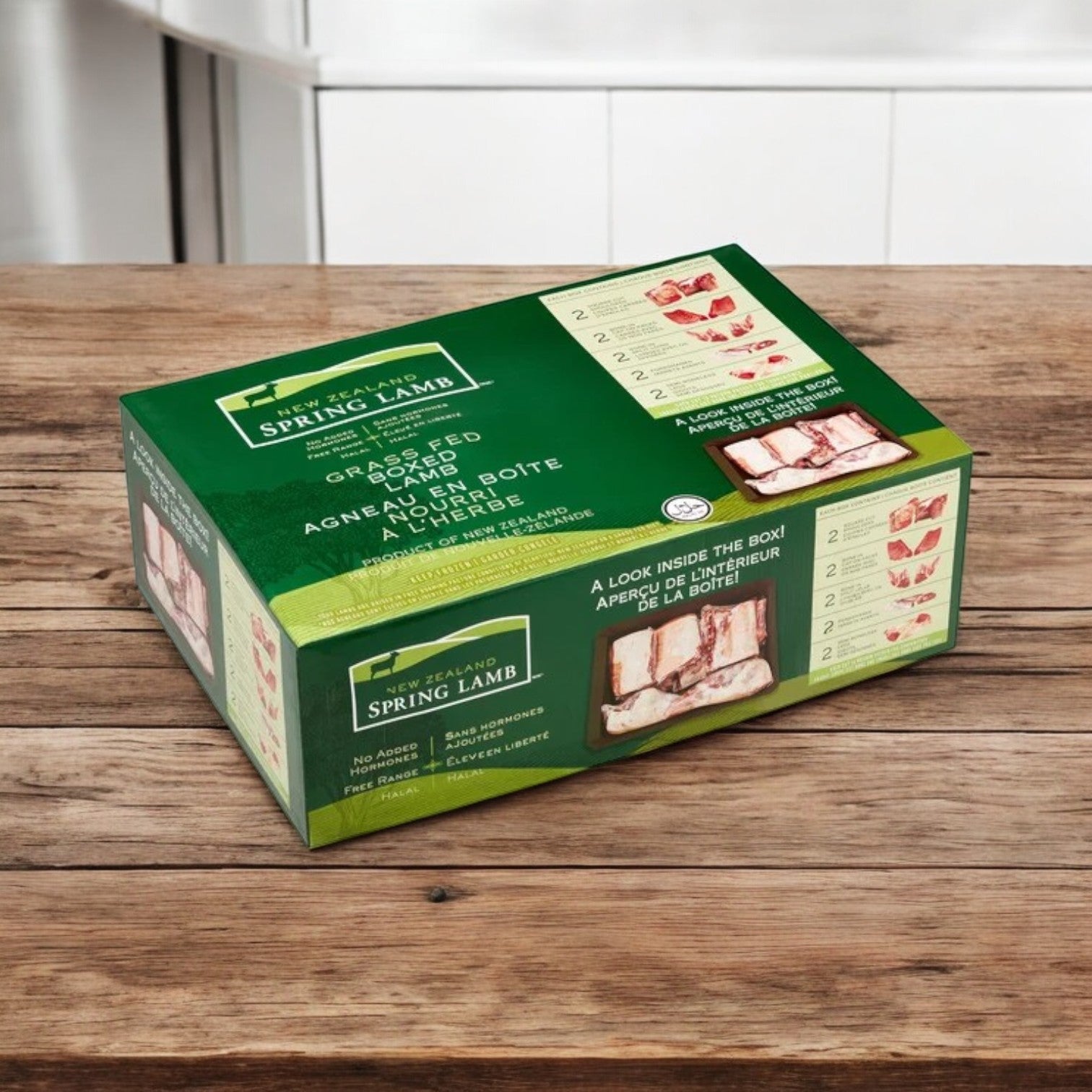 A green box of New Zealand Spring Lamb Halal Lamb Carcass, 8-Way Cut (28 lb avg wt), rests on a wooden countertop. The packaging highlights grass-fed, high-quality Halal lamb from New Zealand with preparation instructions.