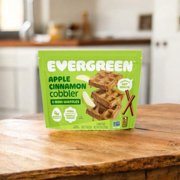 A green bag of Evergreen 3-Pack Combo – Mini Waffles Variety Pack rests on a wooden table, showcasing the frozen convenience ideal for busy mornings in a cozy kitchen.