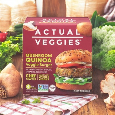 An Actual Veggies Mushroom Quinoa Veggie Burger rests on a wooden table with fresh assorted vegetables. This healthy, protein-packed burger is a nutritious and flavorful choice for a delightful meal.