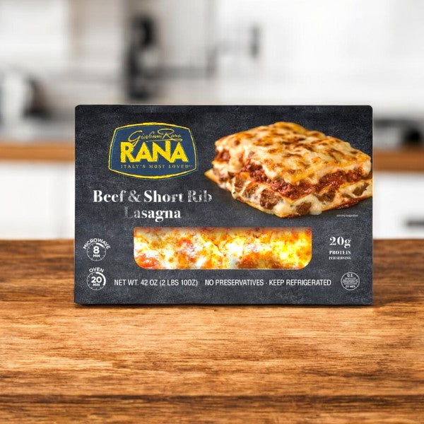 Giovanni Rana Beef & Short Rib Lasagna, 42 oz ready-made meal is displayed on a wooden surface with a kitchen background. The box emphasizes serving size, protein content, and prep time—showcasing this high-quality pasta dish.