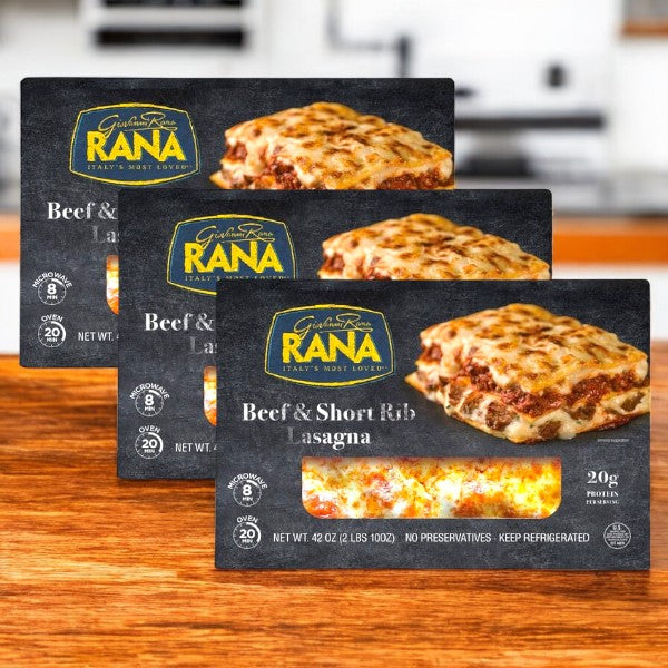 Three packages of Giovanni Rana Beef & Short Rib Lasagna, 42 oz-3 Count, are shown on a wooden surface with a kitchen background.