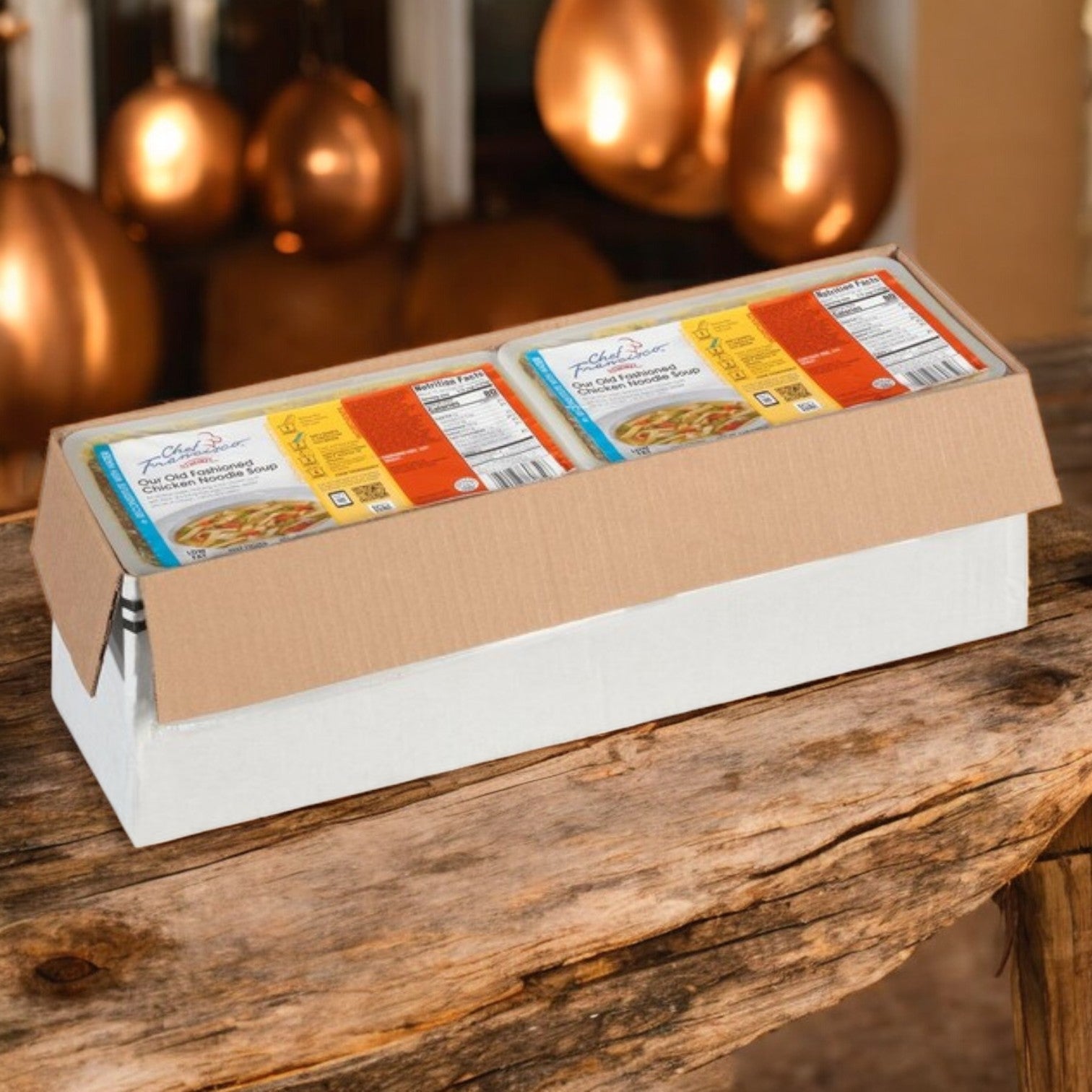 A 64 oz Chef Francisco by Heinz Chicken Noodle Soup box sits on a wooden table with copper-colored lights in the background—ready to heat and serve.