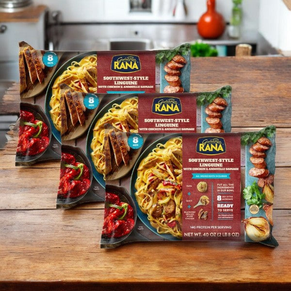 Three 40 oz packages (3 count) of Giovanni Rana Southwest Style Linguine with Chicken and Sausage are shown on a wooden table in a cozy kitchen.
