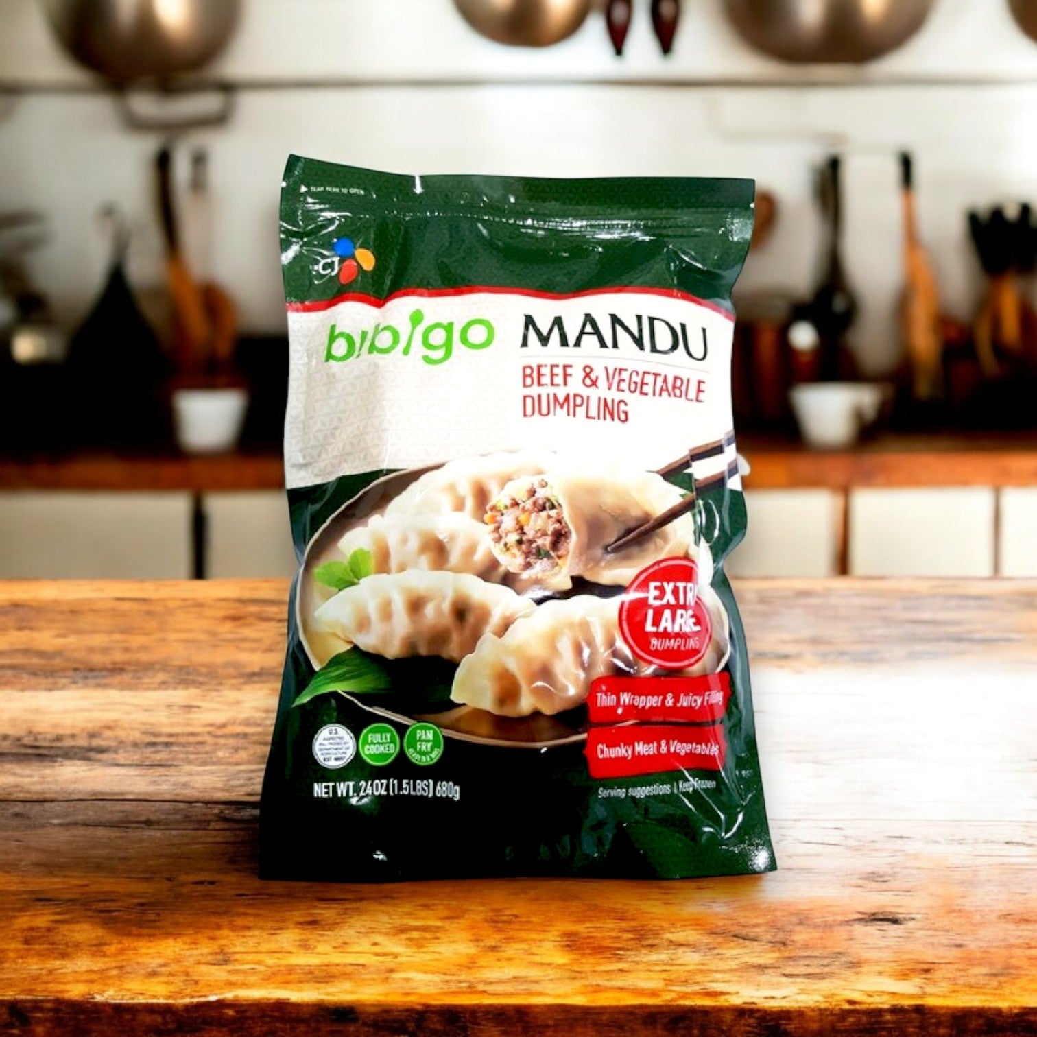 A pack of Bibigo Mandu Beef & Vegetable Dumpling | 24 oz. - 3 Packs sits on a wooden kitchen counter, offering a quick meal solution with authentic Korean flavors from Bibigo against a blurred kitchen backdrop.