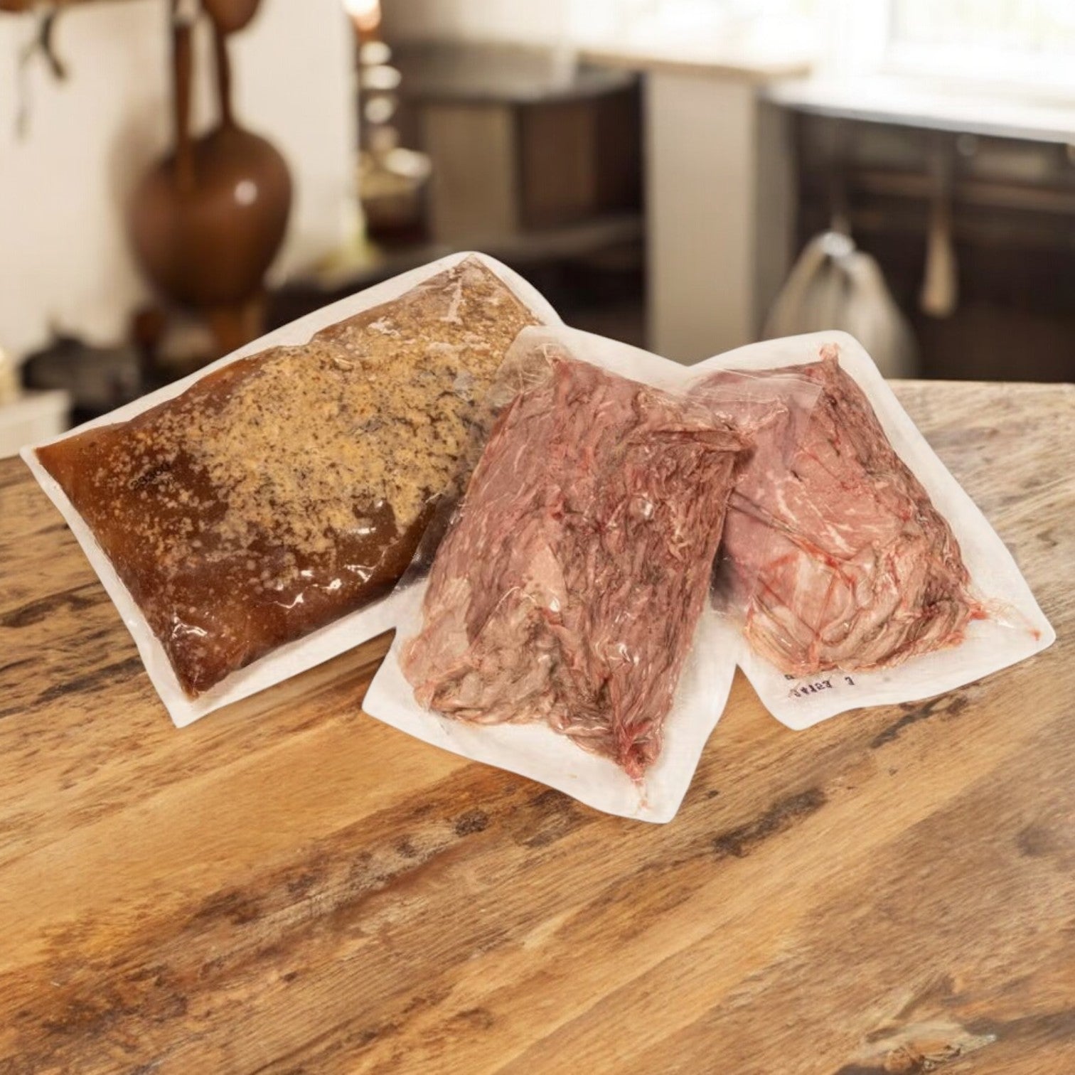Three vacuum-sealed bags of Devanco Sliced Italian-Style Beef with Gravy (10 lb package: 5 lb beef, 4 lb gravy) are placed on a wooden countertop in a kitchen setting.