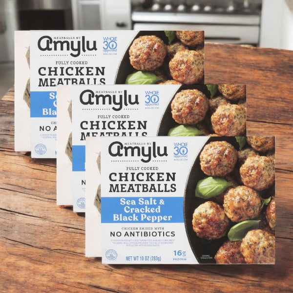 Three boxes of Amylu Chicken Meatballs, Sea Salt & Cracked Black Pepper flavor, sit on a wooden table with "No Antibiotics," "16g Protein," and "Gluten-Free" labels, offering a convenient and healthy meal option.