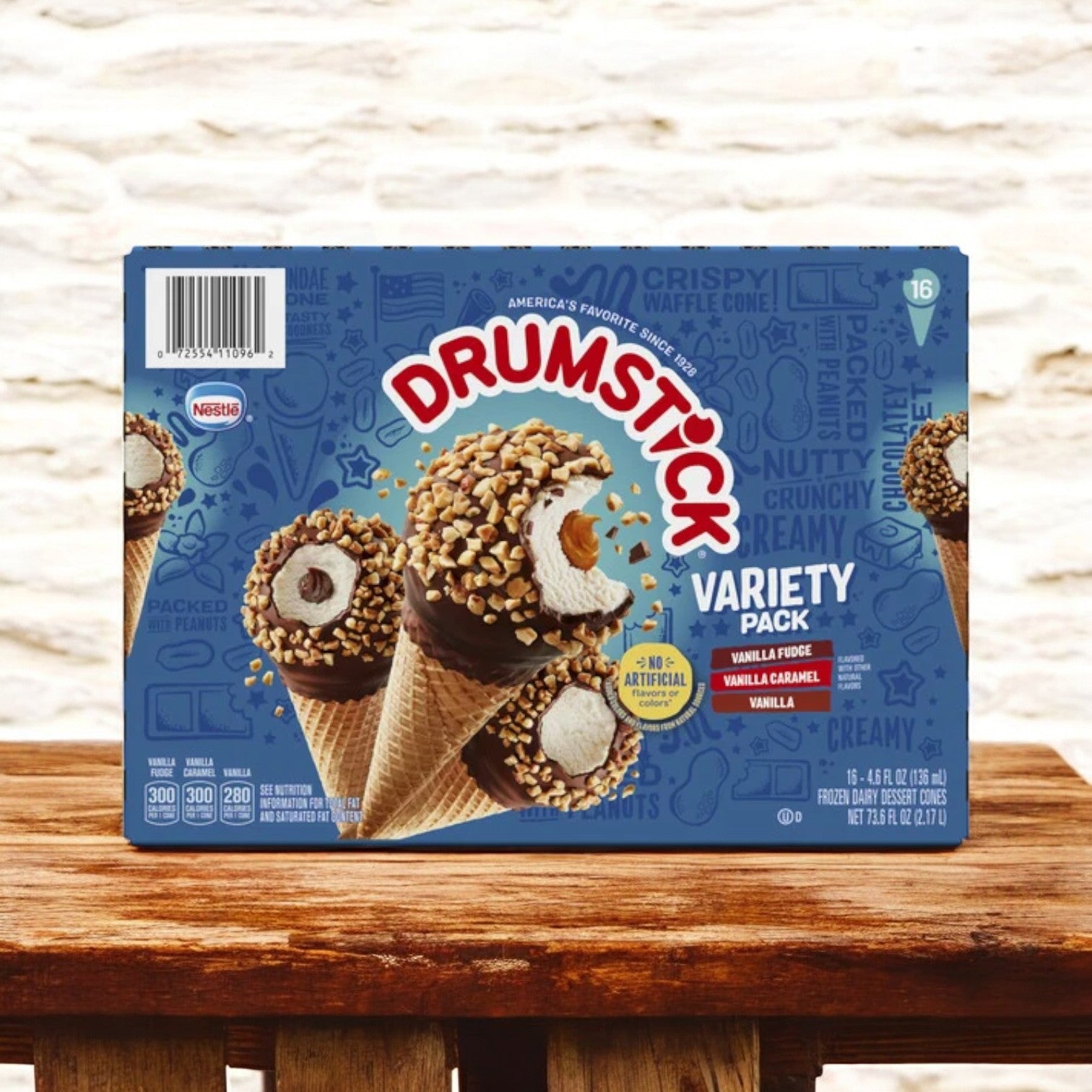 A Nestle Drumstick Cone Variety Pack, Frozen 16 ct. box sits on a wooden surface, displaying three tempting cone flavors on the Nestle-branded packaging.